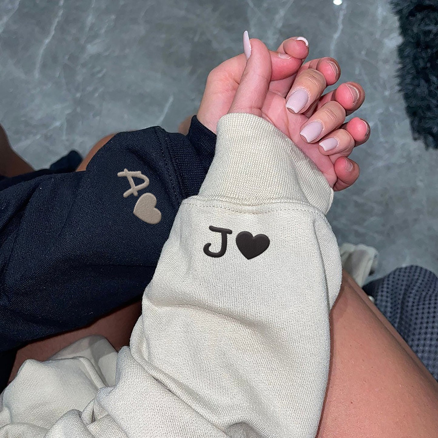 Couple holding hands while showing embroidered initials and hearts on their sleeves