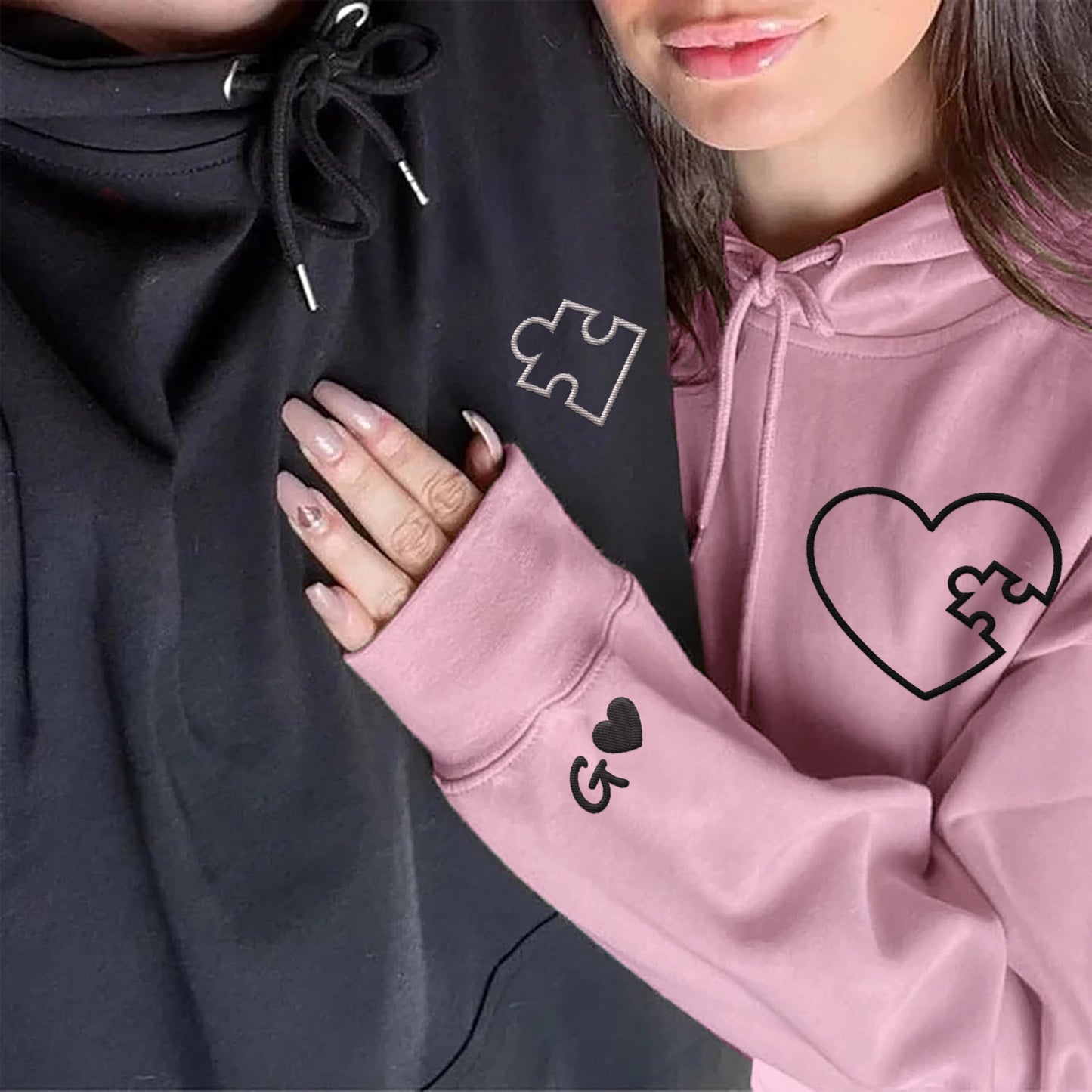 Couple wearing matching black and pink hoodies with embroidered puzzle heart design and personalized initials