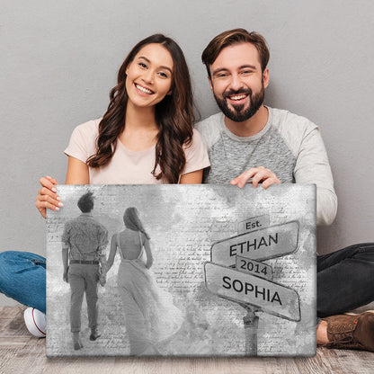 Couple holding a canvas of themselves faced backwards next to the street sign with their names and date