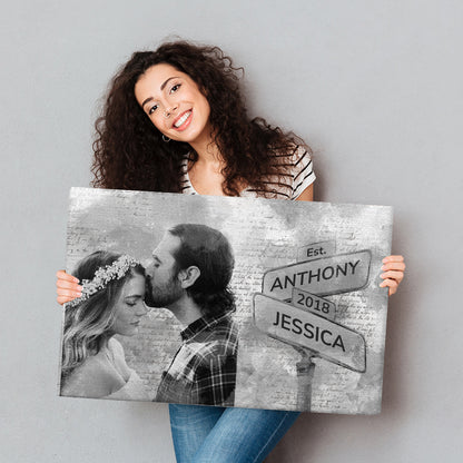 Model holding a canvas of a man kissing a woman next to the street sign with their names and date